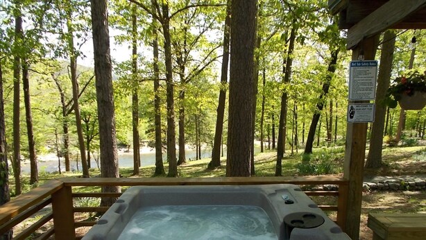 A hot tub surrounded by a wooden deck with a view of a forest and a lake.