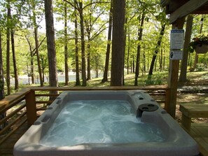 A hot tub surrounded by a wooden deck with a view of a forest and a lake.