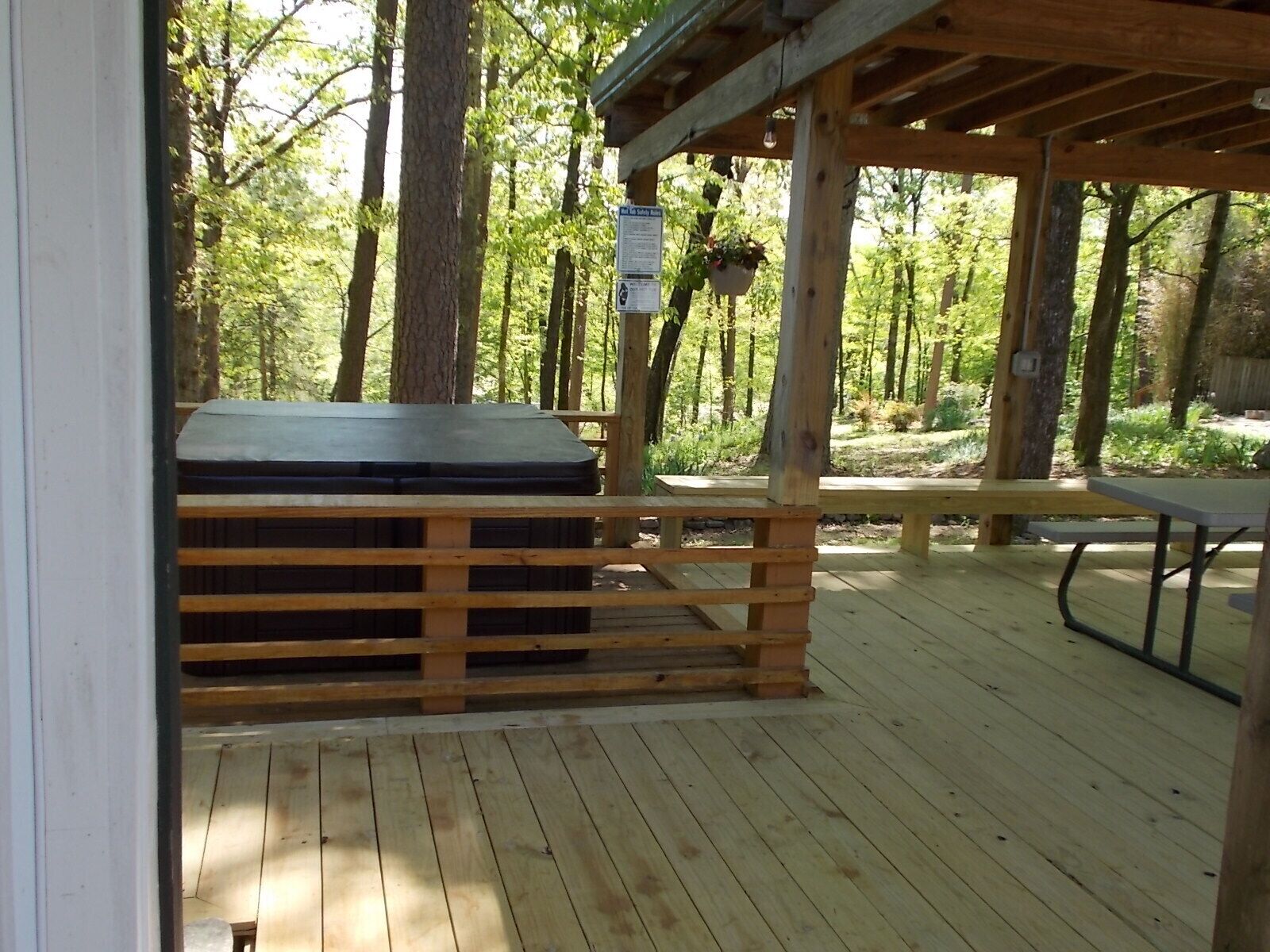 Une terrasse en bois avec un jacuzzi, une table de pique-nique et un panneau indiquant une zone de sécurité.