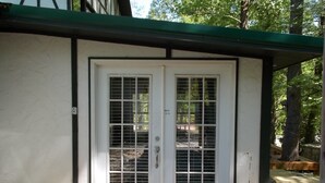 A white door with a metal grill, a small porch area, and a stone pathway leading to the door.