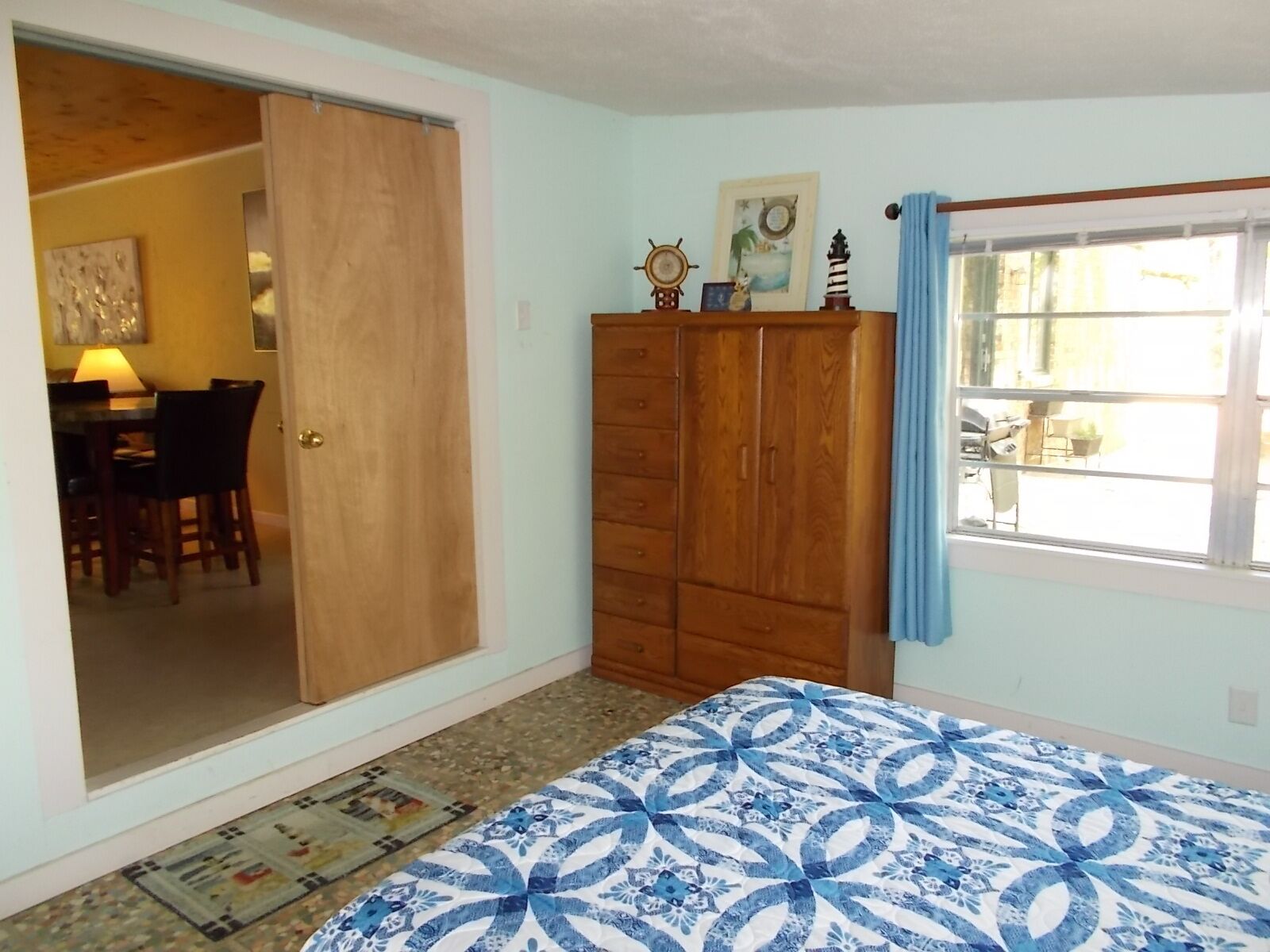 A bedroom with a bed, a wardrobe, a door leading to a dining area, and a window with curtains.