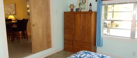 A bedroom with a bed, a wardrobe, a door leading to a dining area, and a window with curtains.