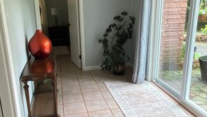 A hallway with a tiled floor, a wooden bench, a potted plant, and a door leading to another room.