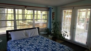 A bedroom with a bed, a window, a door, and a potted plant.