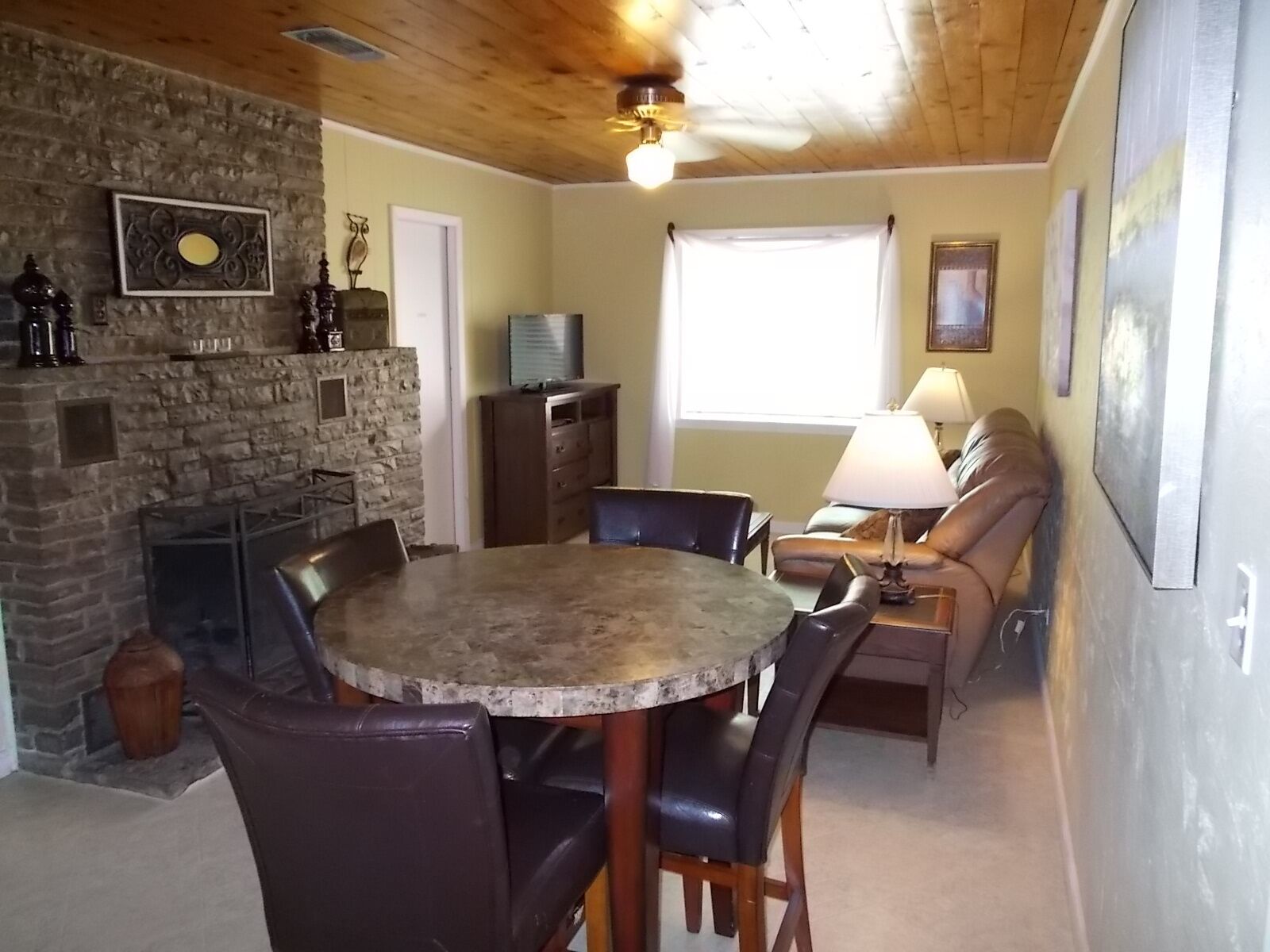 A cozy living room with a stone fireplace, a round dining table, and a comfortable seating area with a sofa and chairs.