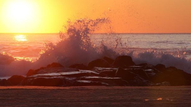 Un atardecer sobre el océano con olas rompiendo contra las rocas.