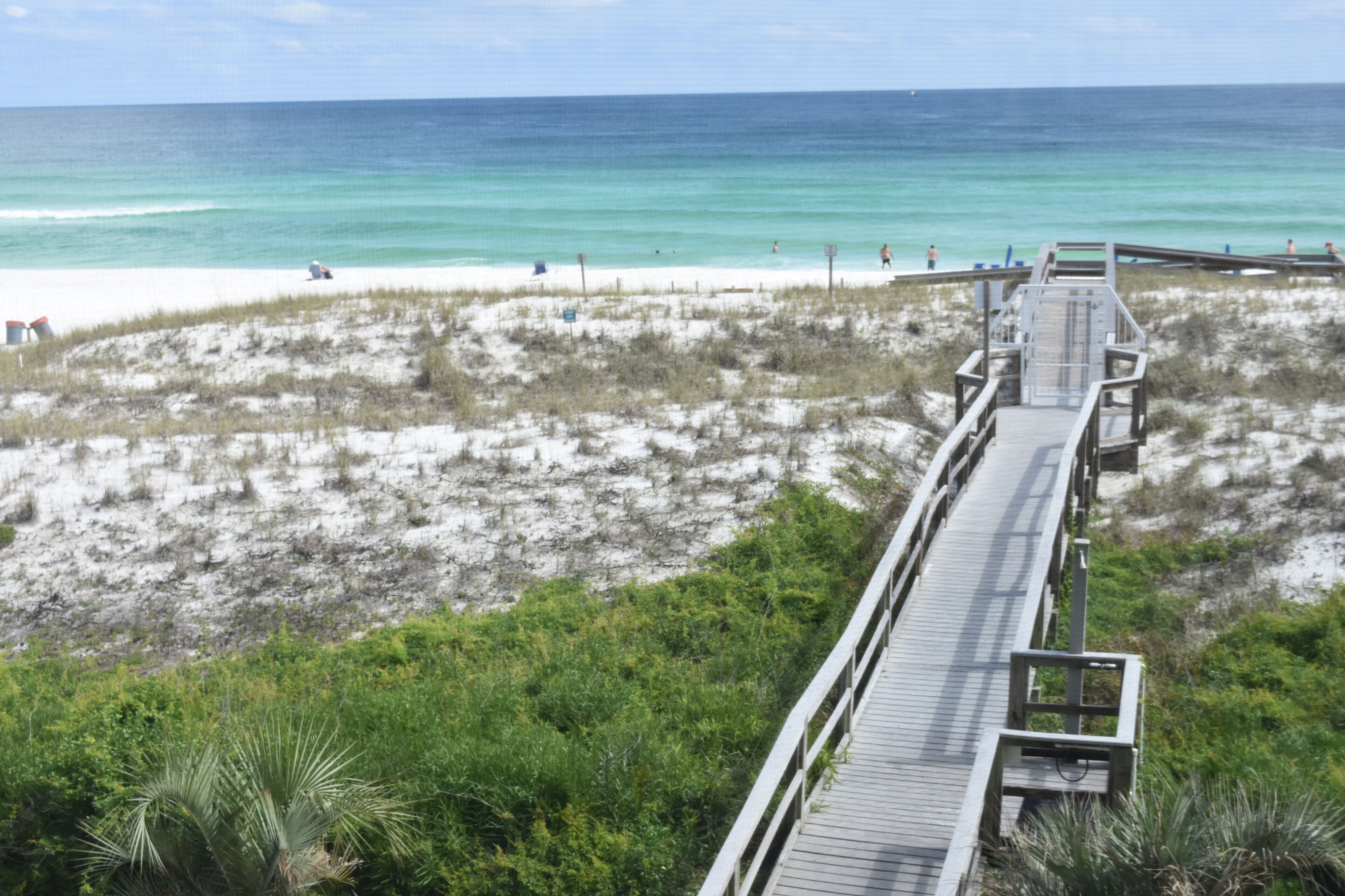 A wooden boardwalk leading to a beach with white sand and clear blue water.