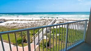 Un balcon avec vue sur une plage, une promenade en bois et quelques plantes.