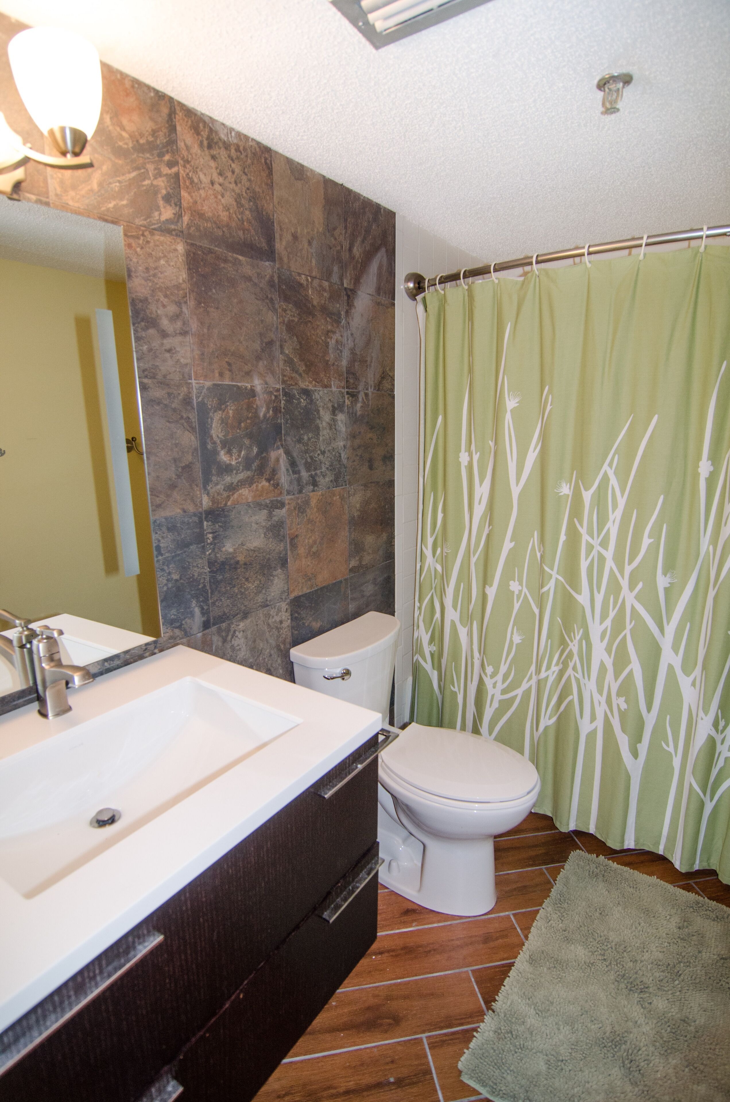 A bathroom with a stone wall, a white sink, a toilet, and a green shower curtain.