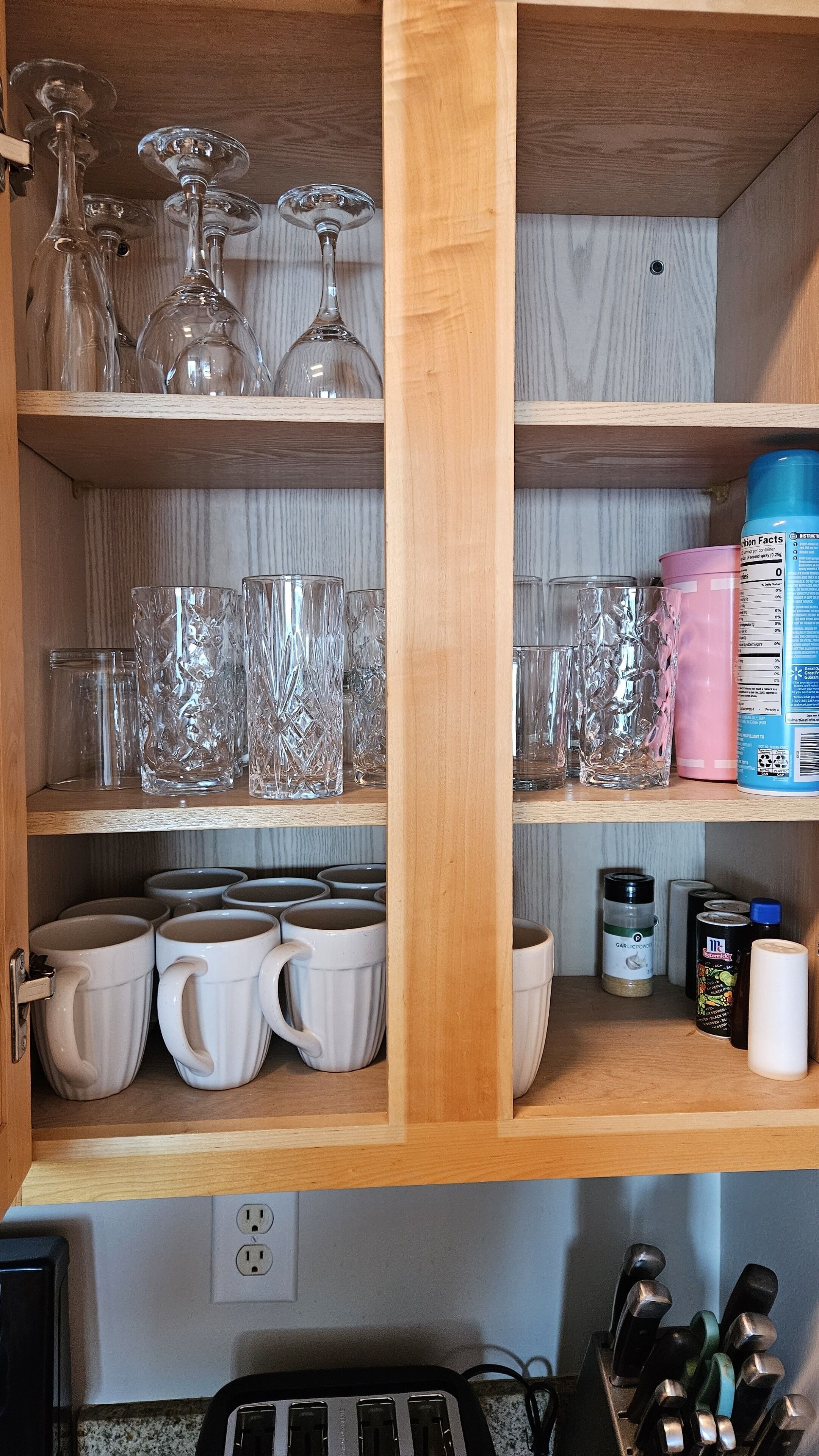 A kitchen with wooden shelves holding various glassware, white mugs, and kitchen essentials like a canister and a container.