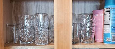 A kitchen with wooden shelves holding various glassware, white mugs, and kitchen essentials like a canister and a container.
