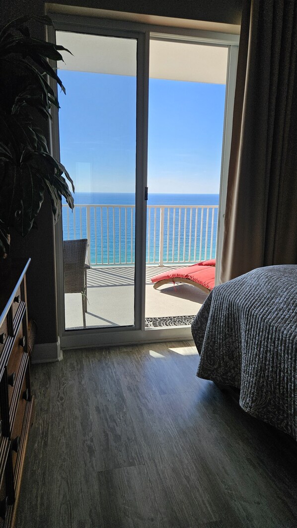A room with a bed, a chair, and a view of the ocean through a sliding glass door.