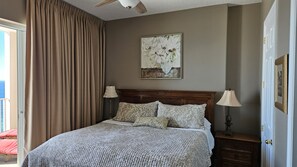Une chambre avec un grand lit, un ventilateur de plafond, un tableau et une table de chevet avec une lampe.