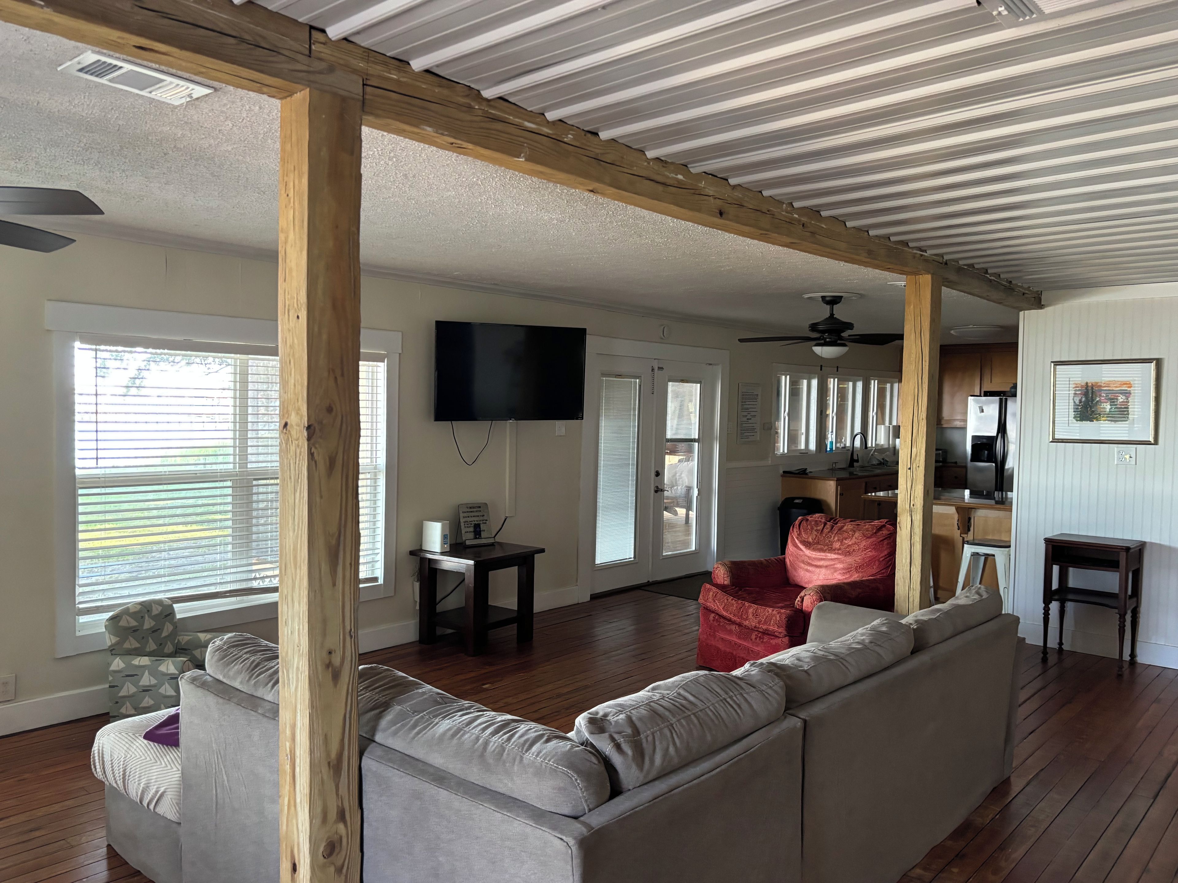 A spacious living area with a grey sofa, a red armchair, and a wooden ceiling structure.