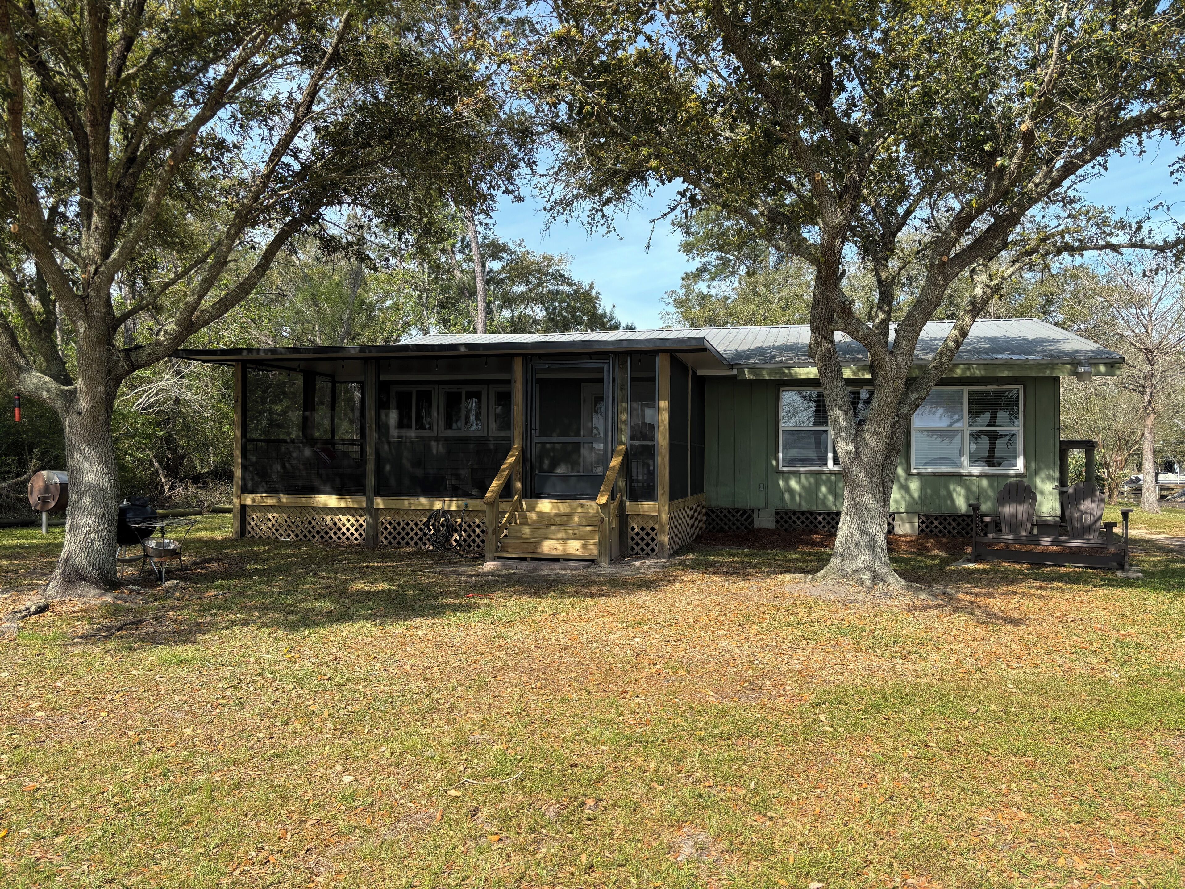 A small, single-story cabin with a porch, surrounded by trees.