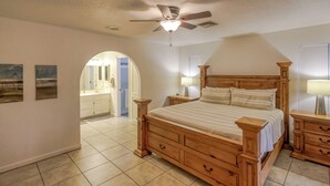 A bedroom with a wooden bed, nightstands, a ceiling fan, and a view to the bathroom. - Tail wags welcome! Close to Lake, Boat and RV Parking! (Lake Havasu City)