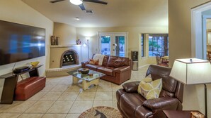 A living room with a flat-screen TV, leather sofas, a glass coffee table, a fireplace, a ceiling fan, and a dining area with a table and chairs. - Tail wags welcome! Close to Lake, Boat and RV Parking! (Lake Havasu City)