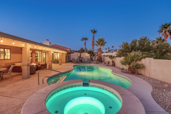 A swimming pool with a curved design, surrounded by a patio area with outdoor furniture and palm trees.