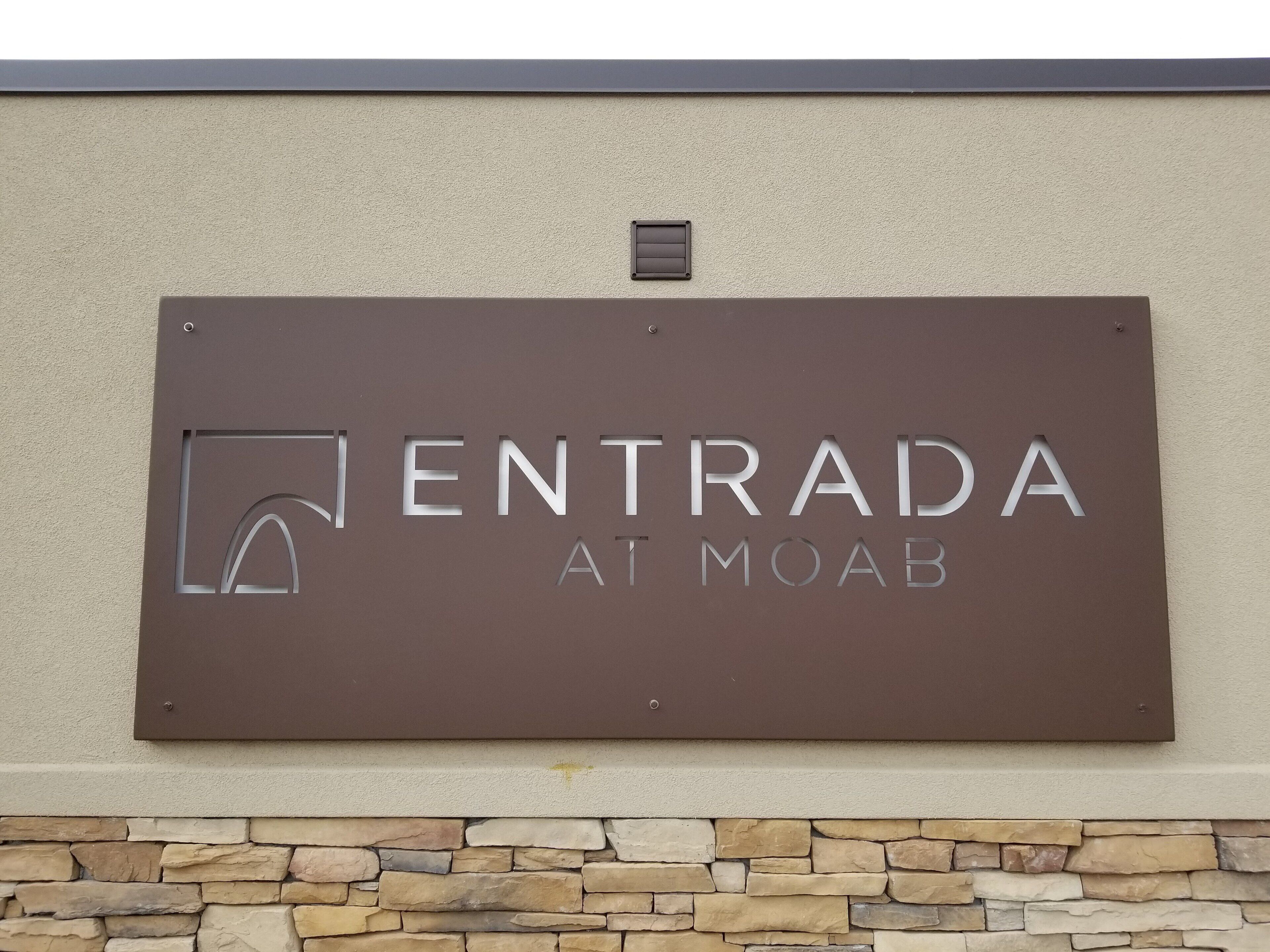 Ein Schild mit dem Aufschrift 'ENTRADA AT MOAB' vor braunem Hintergrund.