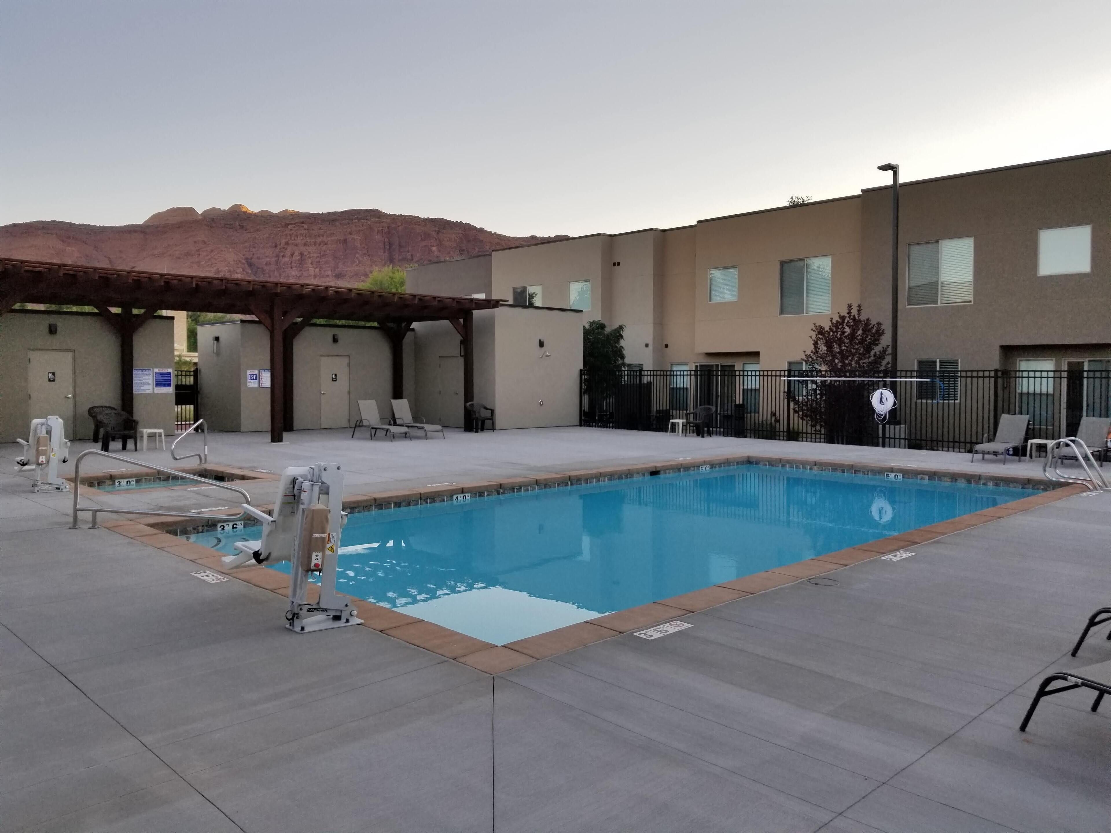 A swimming pool with a lifeguard chair, lounge chairs, and a covered area with a pergola.