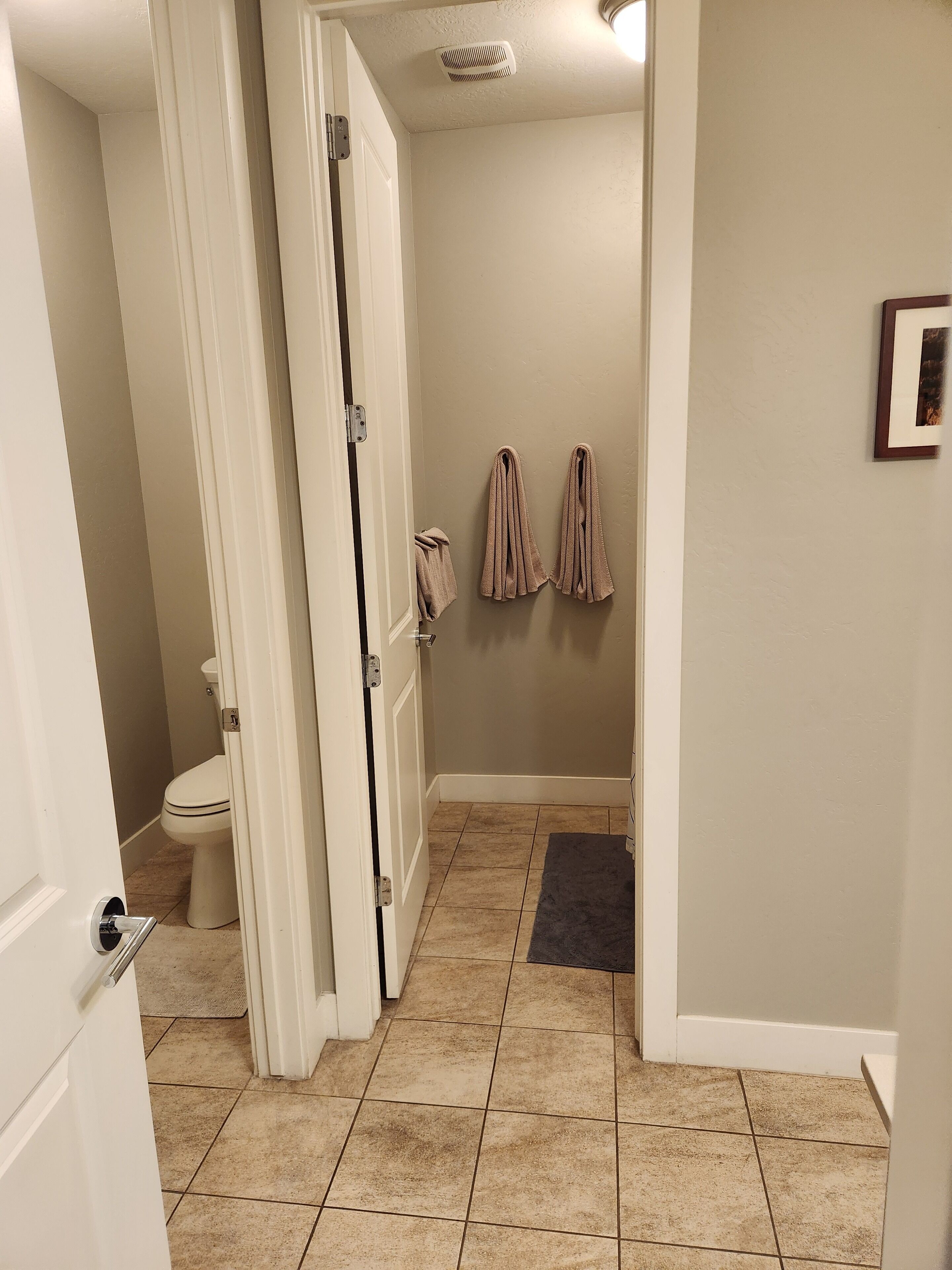 Un baño con inodoro, un perchero con toallas y una puerta que da a otra habitación.