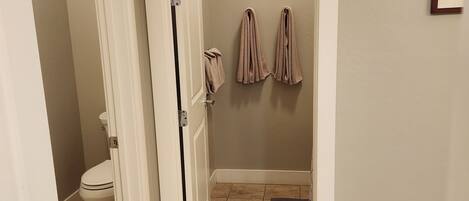 Un baño con inodoro, un perchero con toallas y una puerta que da a otra habitación.