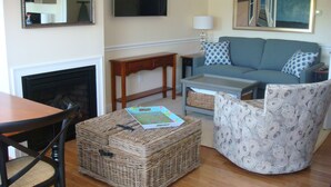 A living room with a fireplace, a sofa, a coffee table, and a wicker ottoman.