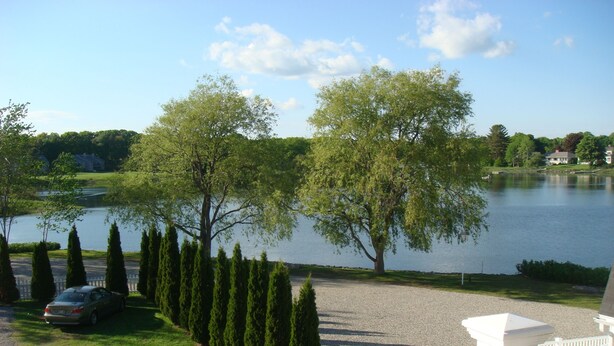 A lakeside property with a gravel driveway, a parked car, and a white railing.