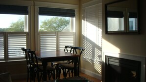 A dining area with a table and chairs, a fireplace, and large windows with blinds.