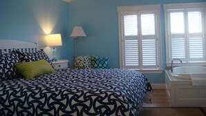 A bedroom with a bed, a nightstand, a lamp, a window with blinds, and a ceiling fan.