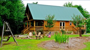 Une cabane en rondins avec un toit végétalisé, une véranda avec des chaises et une balançoire dans le jardin.