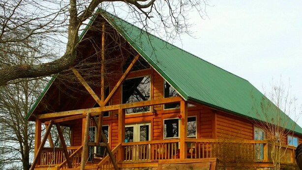 Une cabane en bois avec un toit vert, une véranda et des fondations en pierre.