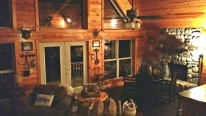 L’intérieur d’un chalet accueillant, avec une cheminée en pierre, des murs en bois et un ventilateur de plafond.