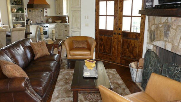 A living room with a brown leather sofa, a tan armchair, and a coffee table. A stone fireplace is visible in the background. - Villa della Luna, an authentic Tuscan Villa in Montaluce, license #3857 (Dahlonega)