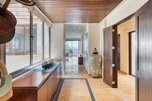 A hallway with a wooden ceiling, a large vase, and a view to a balcony.