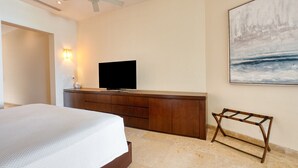 A hotel room with a bed, a flat-screen TV on a wooden dresser, a ceiling fan, and a painting on the wall. - Beach Front Condo w/ Balcony! Amazing Views, White Sand & Pools! (Punta Mita)