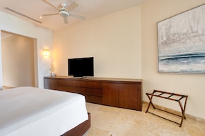 A hotel room with a bed, a flat-screen TV on a wooden dresser, a ceiling fan, and a painting on the wall. - Beach Front Condo w/ Balcony! Amazing Views, White Sand & Pools! (Punta Mita)
