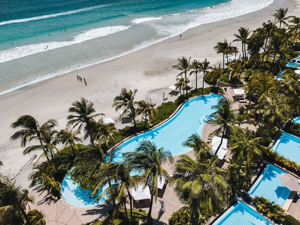 A resort with a large pool surrounded by palm trees and a beach. - Beach Front Condo w/ Balcony! Amazing Views, White Sand & Pools! (Punta Mita)