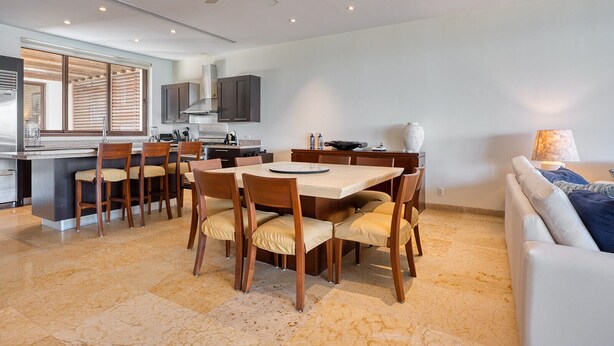 A modern kitchen with dark cabinets, a central island, and a dining area with wooden chairs and a table. - Beach Front Condo w/ Balcony! Amazing Views, White Sand & Pools! (Punta Mita)