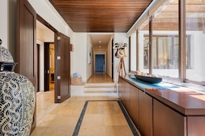 A hallway with a wooden ceiling, a marble floor, and a view through large windows.