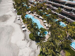 Un complexe hôtelier doté d’une piscine entourée de palmiers et offrant une vue sur la plage.