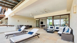 A sunlit outdoor lounge area with lounge chairs, a sofa, and a television. - Beach Front Condo w/ Balcony! Amazing Views, White Sand & Pools! (Punta Mita)