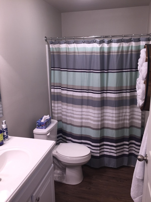 A bathroom with a striped shower curtain, a toilet, and a sink with soap dispensers.