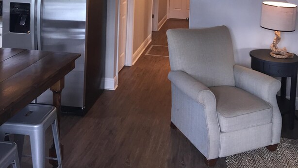 A modern kitchen with a stainless steel refrigerator, wooden dining table, and a chair. A staircase leads to a second floor with a wooden railing.