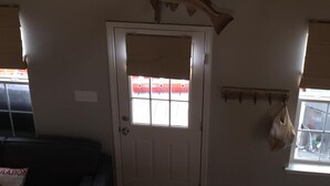 A room with a white door, a fish mounted on the wall, a bag hanging on a hook, and a window with blinds.