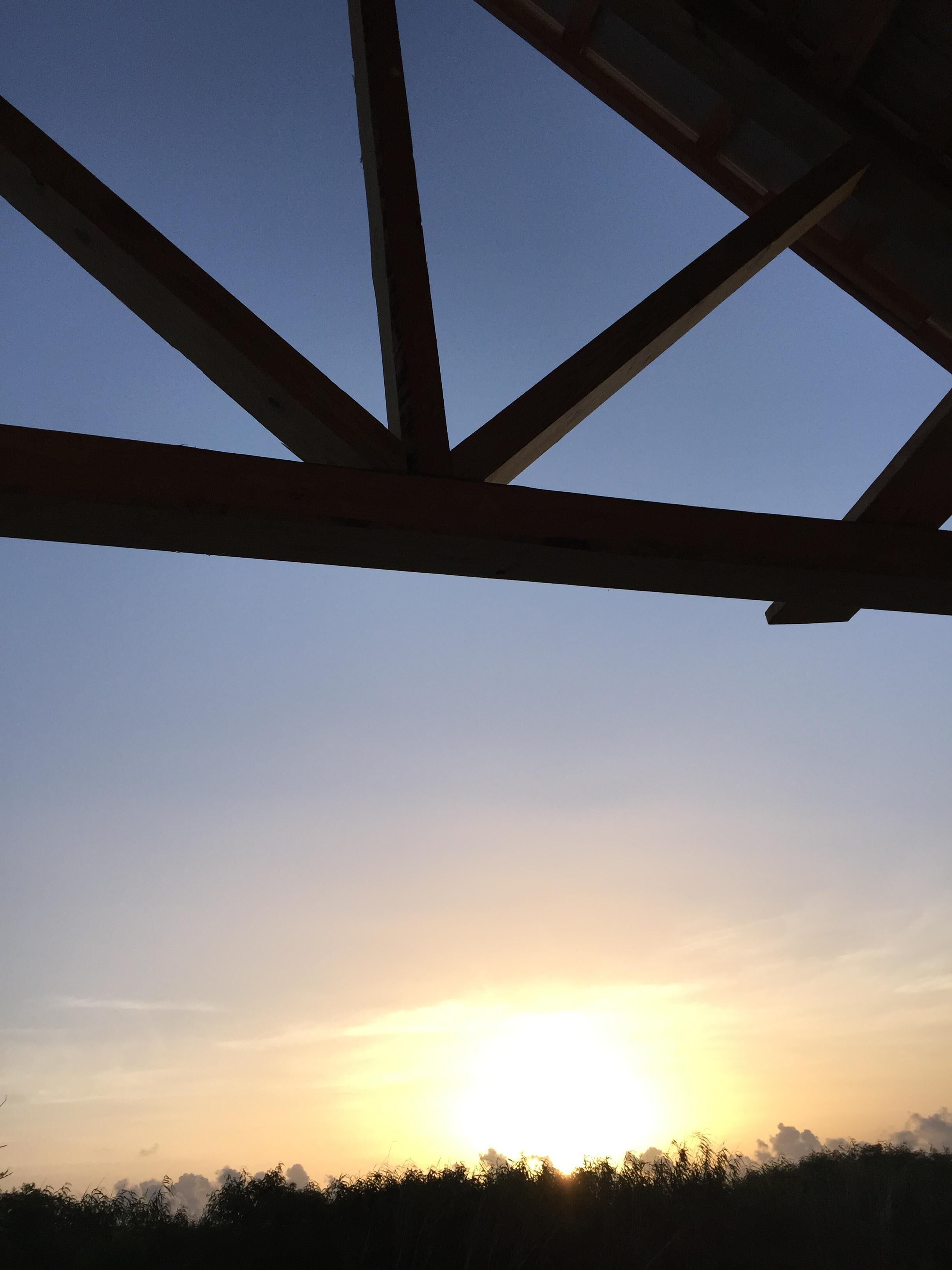 A sunset viewed through a wooden structure with beams.