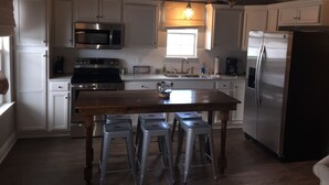 A kitchen with white cabinets, stainless steel appliances, a wooden table, and bar stools.