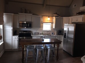 A kitchen with white cabinets, stainless steel appliances, a wooden table, and bar stools.