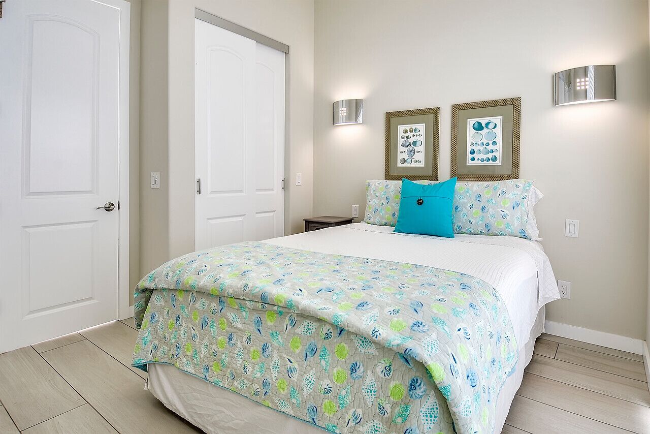 A bedroom with a bed, two wall-mounted light fixtures, and two framed pictures on the wall.