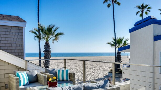 Ein Balkon mit Korbmöbeln, einem Glastisch und Blick auf Strand und Meer.